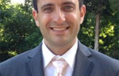 Jeremy smiles wearing blazer and tie, trees behind